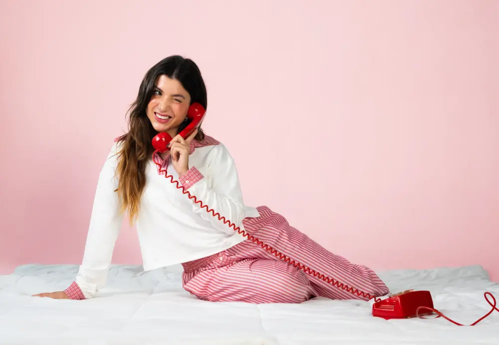 Modelo com conjunto da Frambô e uma sacola vermelha da marca, em fundo rosa.